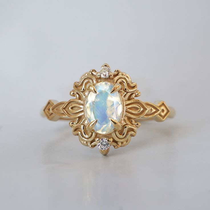 Read about our payment plans before proceeding. In the heart of this exquisite Faith ring, a magical moonstone with a blue sheen nestles, a gem of nature's tender artistry. Embraced by delicate scroll-like motifs, each curve whispers tales of timeless elegance, bestowing upon it a vintage flair that dances with the echoes of ages past. Crafted by skilled hands, this ring is available in your choice of 14K and 18K yellow gold, rose gold, and white gold. All orders come in our Tippy Taste ring box. This ring is handmade and designed in NYC. 14K or 18K solid gold Natural moonstone, 6*4mm Natural round diamonds. SI clarity, GH color, 0.02ct total carat weight 1.5mm ring band ** Tippy Taste Heirloom Collection is made to order. Please allow 3-4 week turnaround time. Shipping:Domestic: Free ship Heirloom Moonstone Ring With Rose Cut Diamonds For Promise, Heirloom Style Moonstone Ring With Rose Cut Diamonds, Heirloom Moonstone Ring With Rose Cut Diamonds, Heirloom Gold Moonstone Ring, Heirloom Moonstone Promise Ring, Celestial 14k Gold Opal Gemstone Ring, Heirloom Moonstone Ring For Anniversary, Handmade 14k Gold Oval Moonstone Ring, Heirloom 14k Gold Moonstone Ring For Anniversary