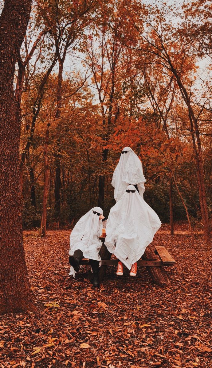 two people dressed up as ghostes sitting on a bench in the middle of a forest