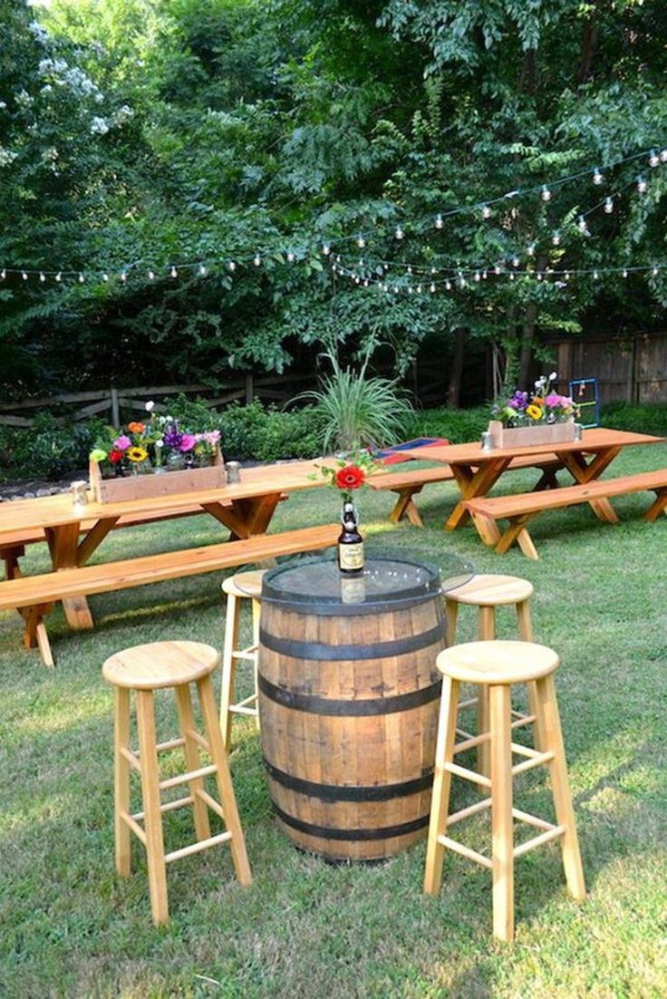 an outdoor table with several wooden barrels and stools in the grass next to picnic tables