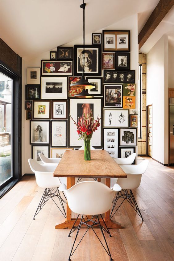 a wooden table surrounded by white chairs in front of a wall with pictures on it