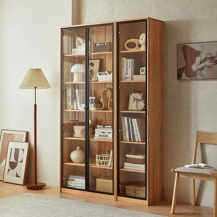 a bookcase with glass doors in a living room next to a chair and lamp