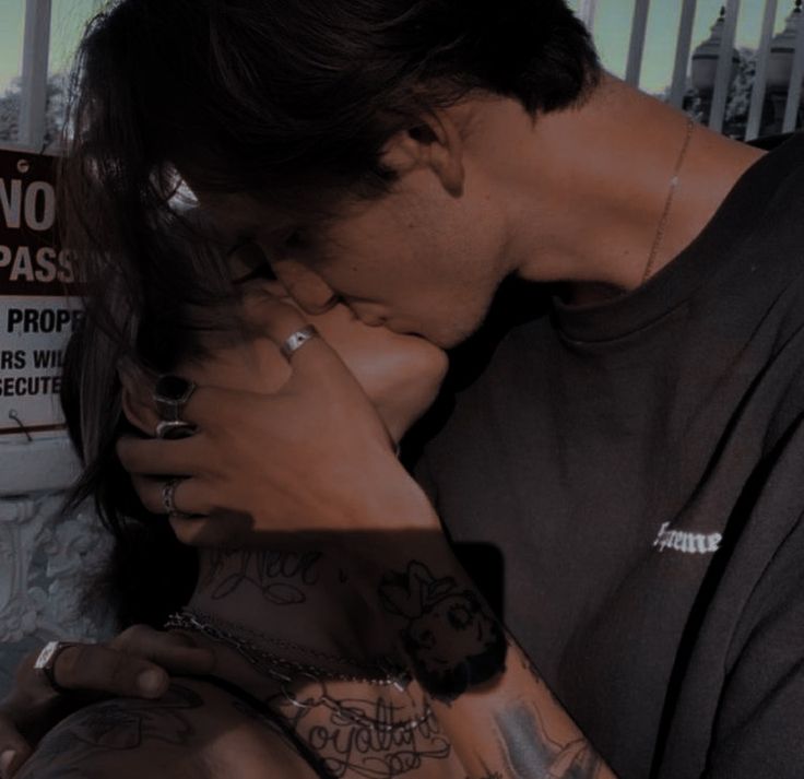 a man and woman kissing each other in front of a fence with graffiti on it