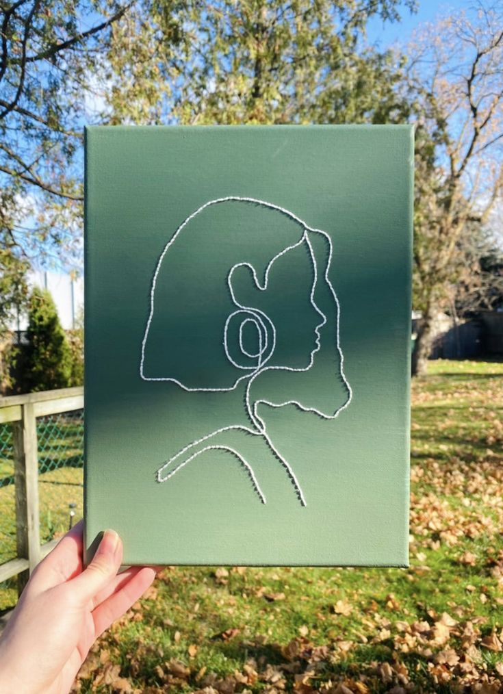 a hand holding up a drawing of a woman's head in front of a fence