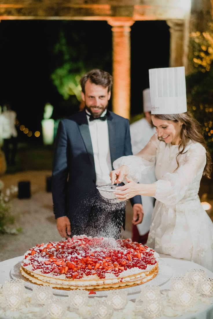 a man and woman are standing in front of a large pizza that is covered with strawberries