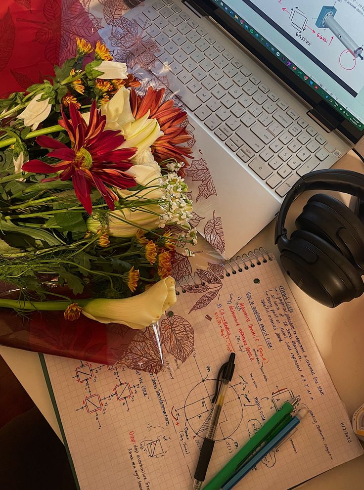 an open laptop computer sitting on top of a desk next to a bouquet of flowers