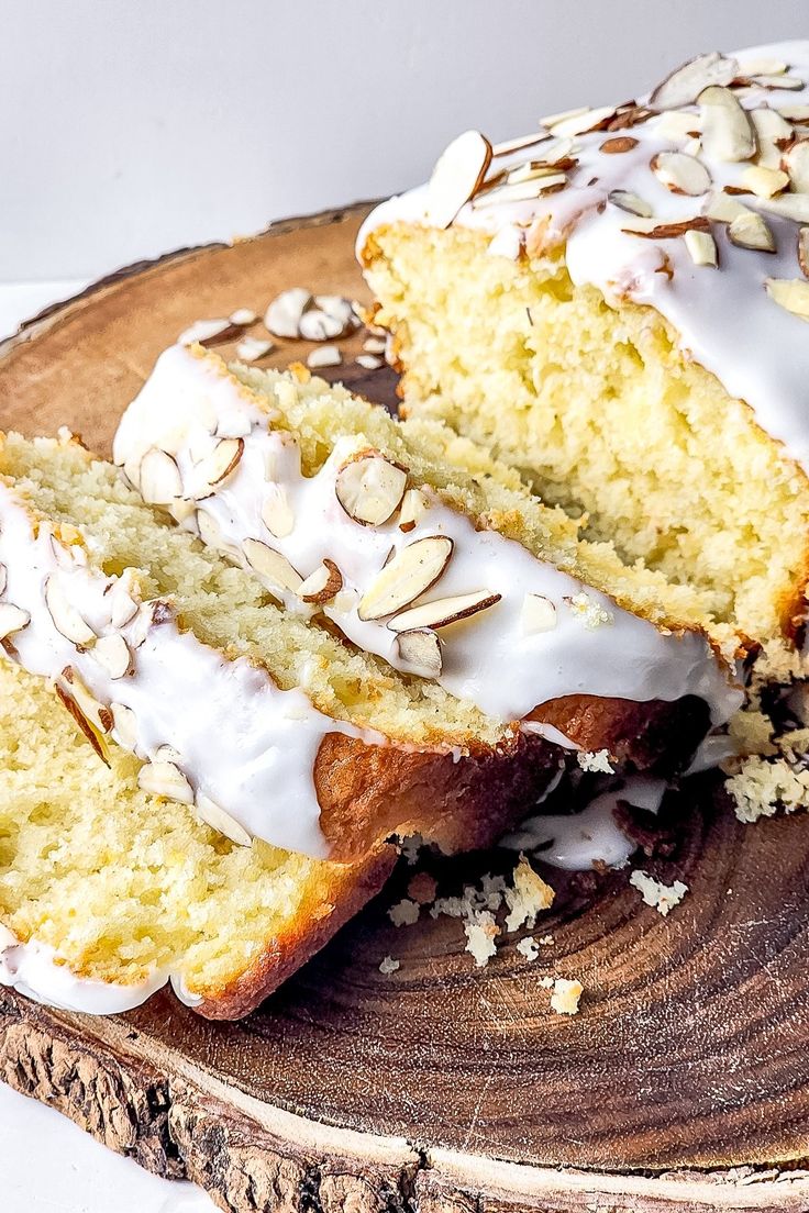 slices of cake with white frosting and almonds sitting on a wooden platter