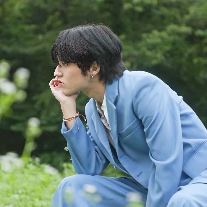 a woman sitting in the grass with her hand on her chin and looking off into the distance