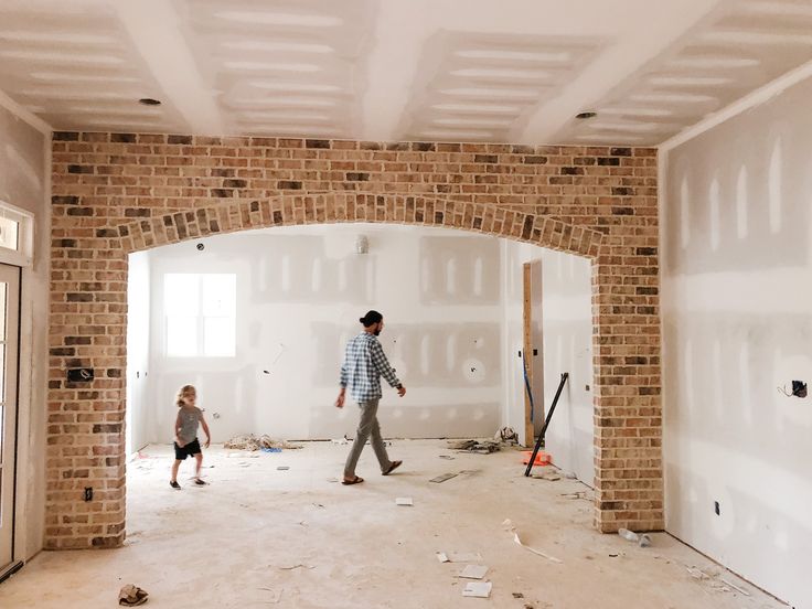 a man and child are walking through an unfinished room with exposed brickwork on the walls