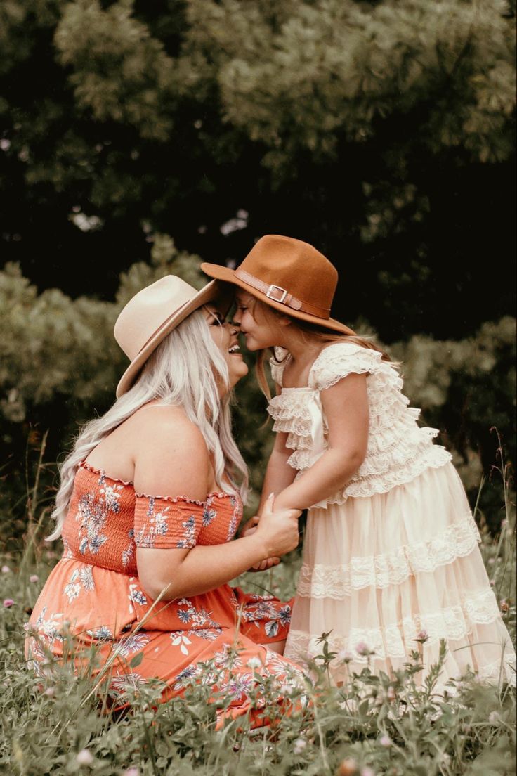 two women are sitting in the grass and one is holding her hand to another woman's face