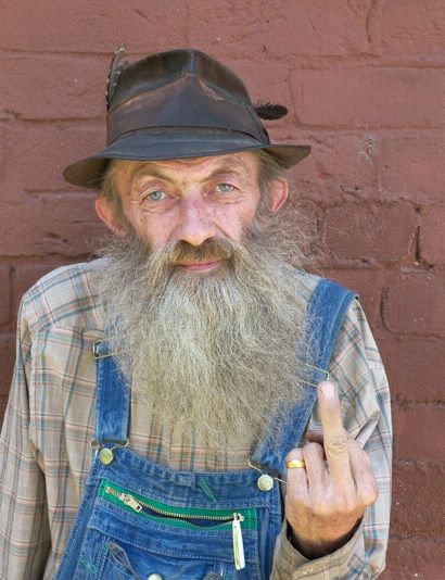 an old man wearing overalls and a hat making the peace sign with his hand