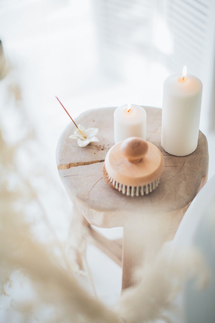 two white candles sitting on top of a wooden table next to a brush and comb