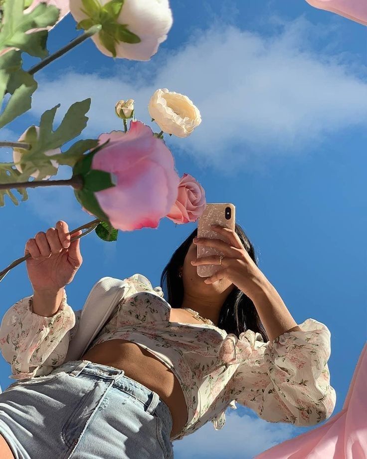 a woman taking a selfie with her cell phone and flowers in the sky behind her