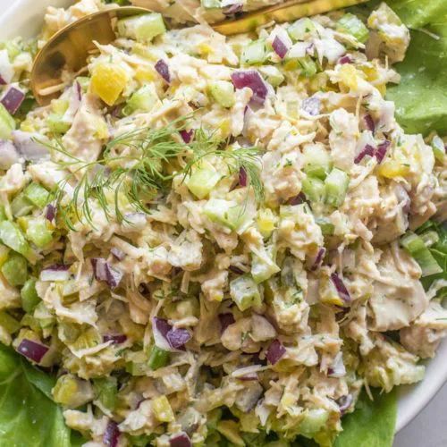 a white bowl filled with salad on top of lettuce and topped with a wooden spoon