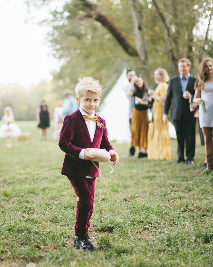 a little boy in a suit and tie holding a frisbee while standing in the grass