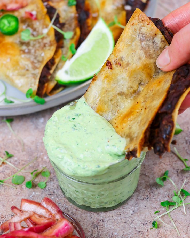 a hand holding a tortilla chip with guacamole in the background