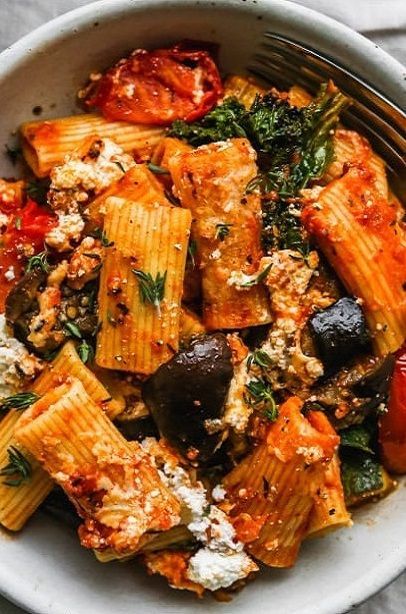 a white bowl filled with pasta, vegetables and fettuccine on top of a table