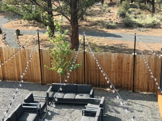 an outdoor seating area with lights strung across the fence and trees in the back ground