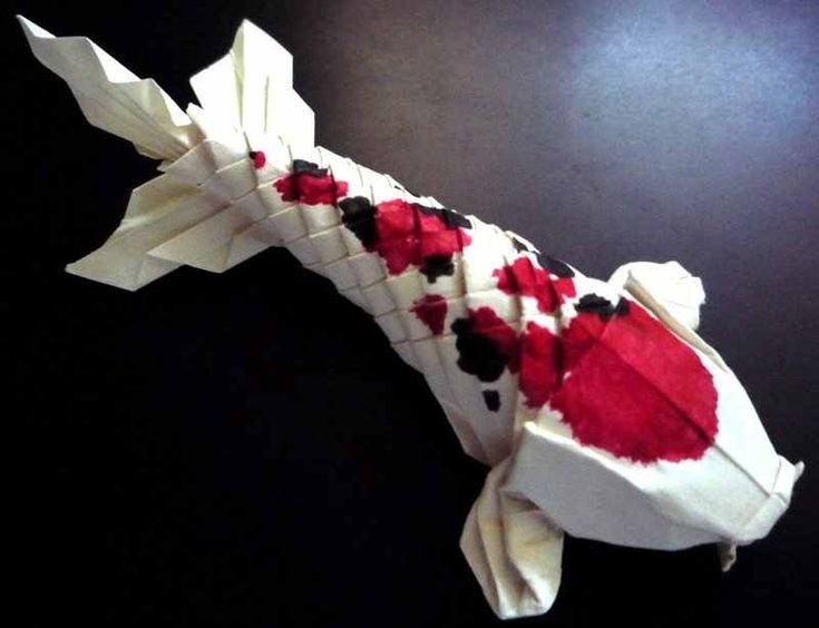 an origami fish with red and black flowers on it's tail, sitting on a table