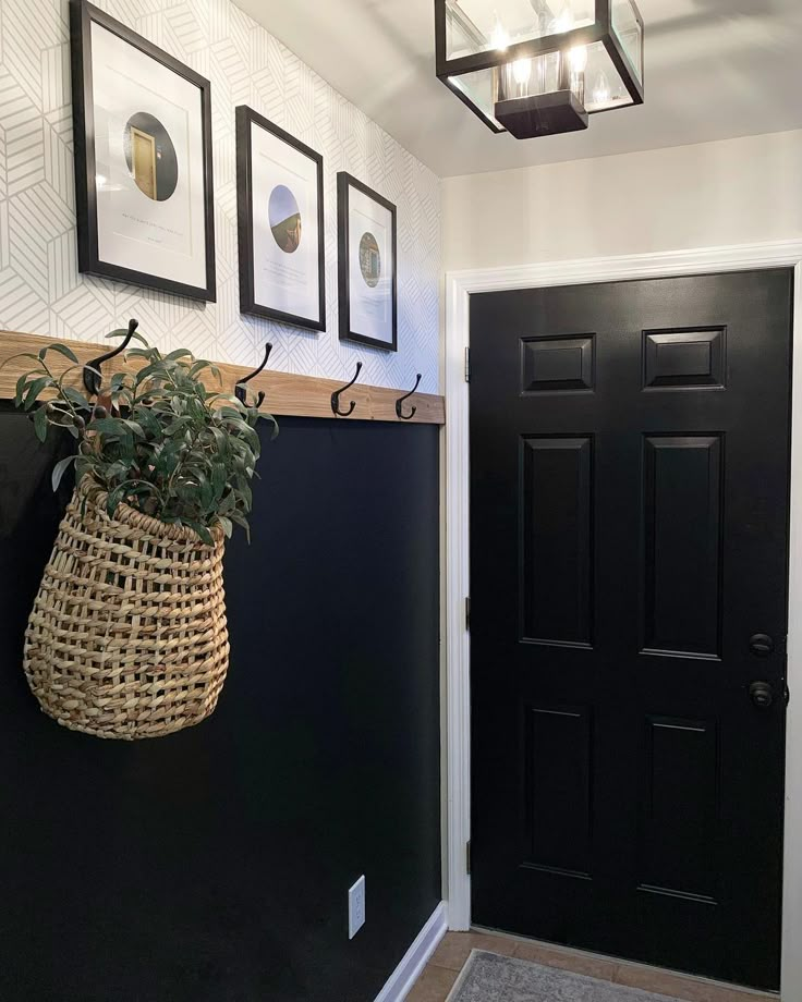 a black front door with a basket hanging from it's side and three framed pictures on the wall