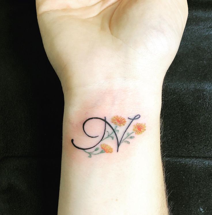 a woman's wrist tattoo with the letter v on it and flowers in the middle