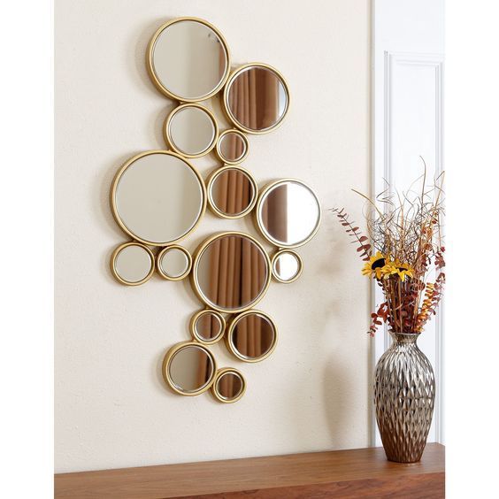 a wall mounted mirror on the side of a wooden shelf next to a vase with flowers