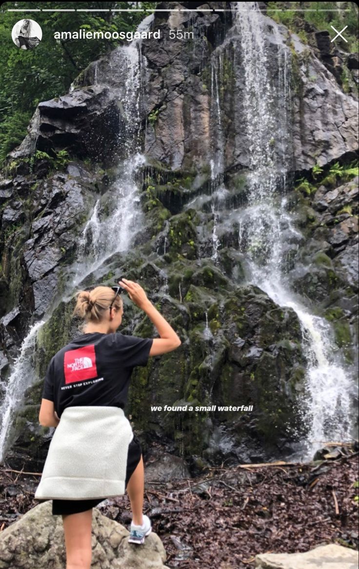 a woman standing in front of a waterfall with her hand on her hip and looking at the water