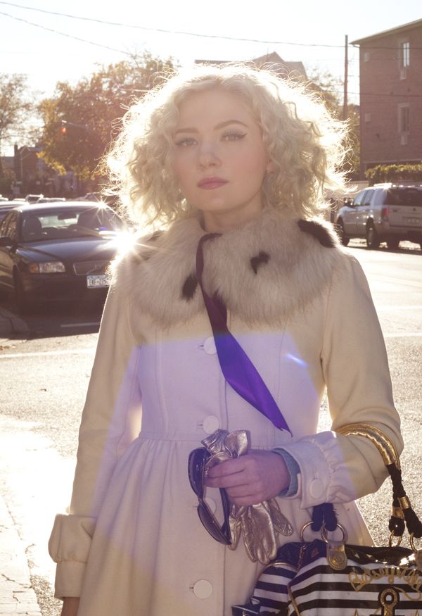 a woman in a white dress and fur collar holding a handbag on the street