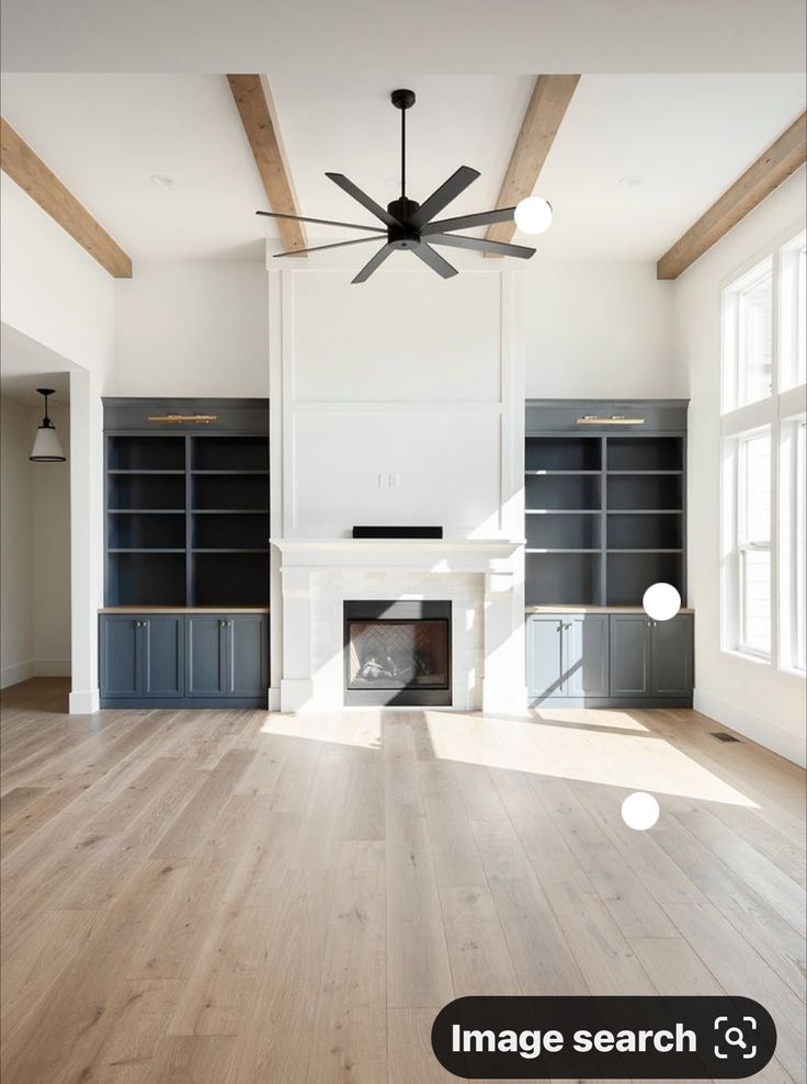 an empty living room with wood floors and ceiling fan in the center, surrounded by built - in bookshelves