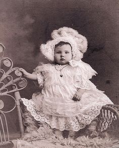 an old fashion photo of a baby in a dress and bonnet with lots of hair