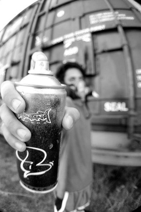 a person holding up a spray can in front of a van with graffiti on it