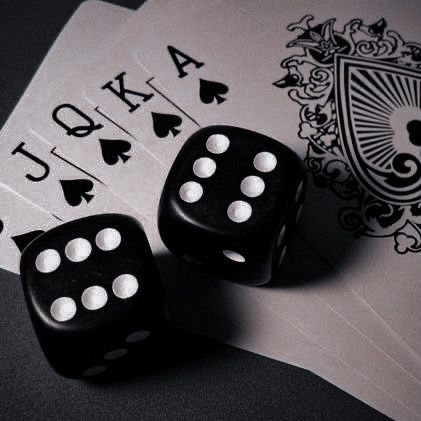 two black dice sitting on top of each other next to playing cards with white dots