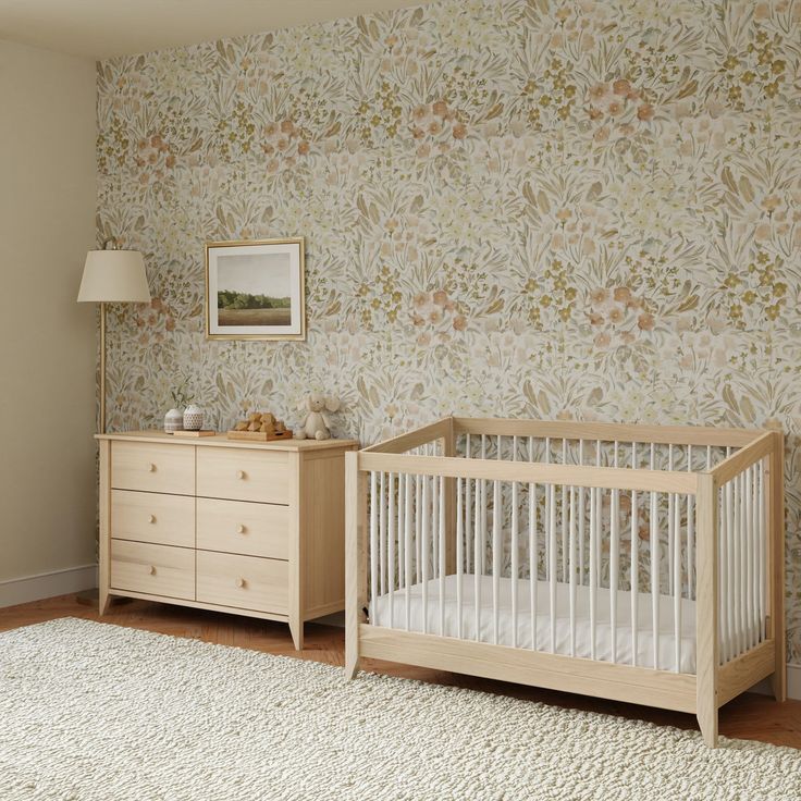 a baby's crib and dresser in a room with floral wallpaper on the walls