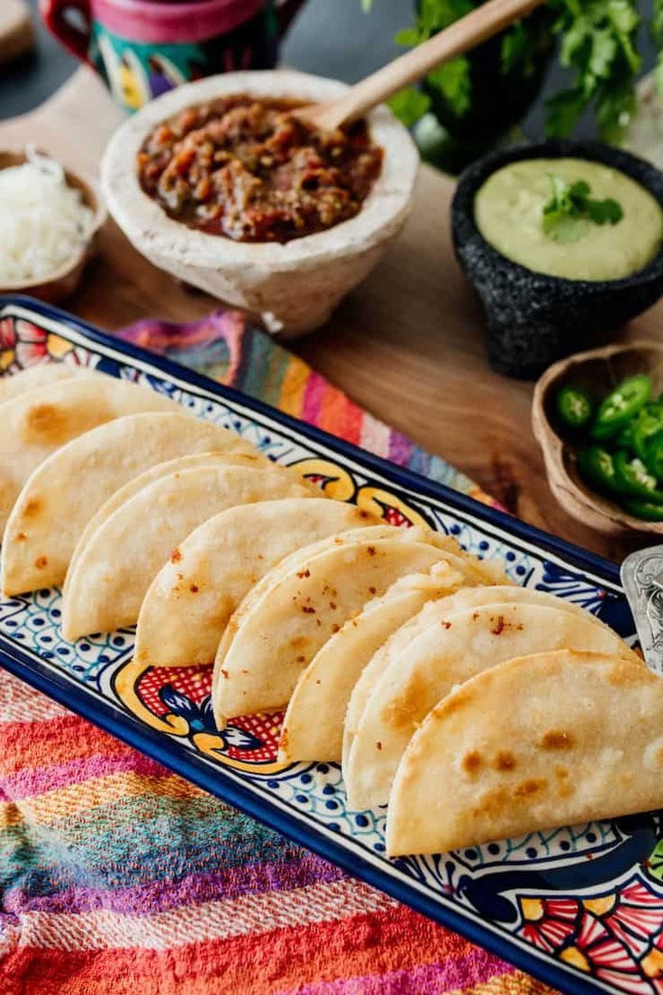 six tortillas on a plate with salsa and guacamole in the background