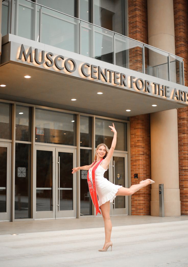 a woman in a white dress and red scarf is dancing outside the museum center for the arts