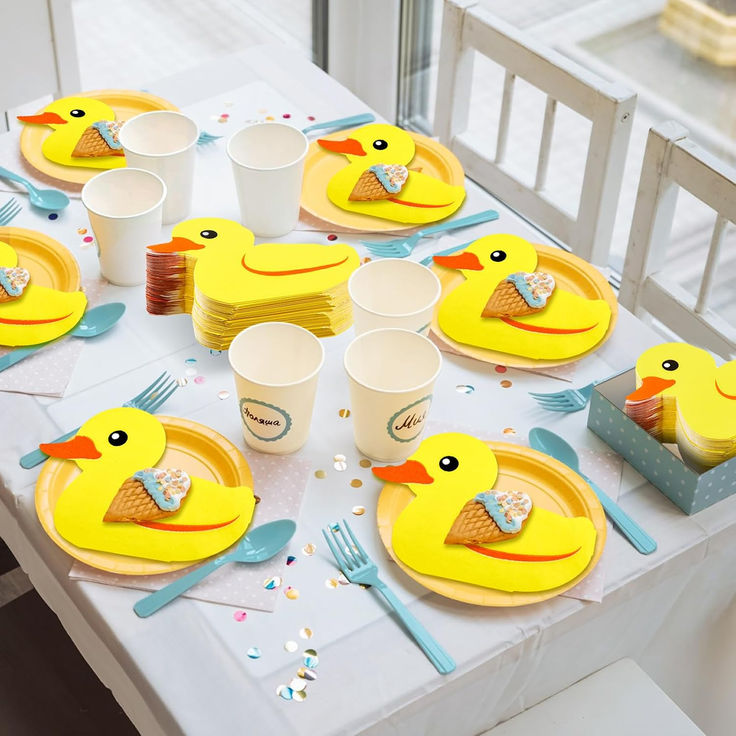 a table set with plates, cups and yellow rubber ducky decorations for a baby's birthday party