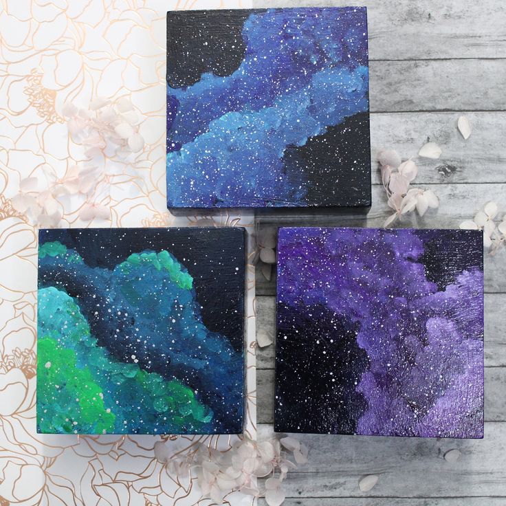 three square paintings with blue, green and purple paint on them sitting on a wooden surface