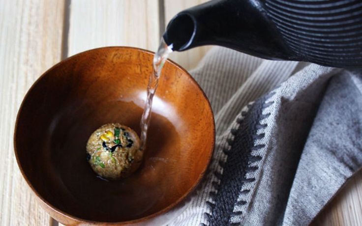 a wooden bowl filled with food on top of a table next to a black kettle