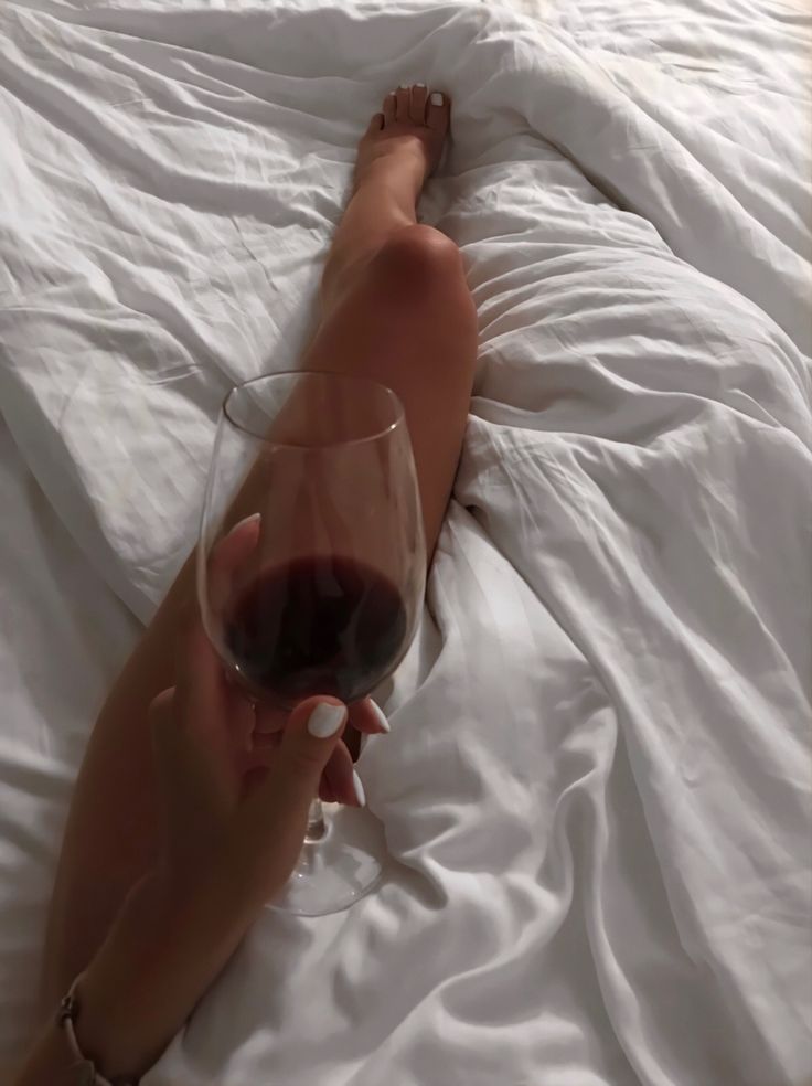 a person laying in bed with a glass of wine