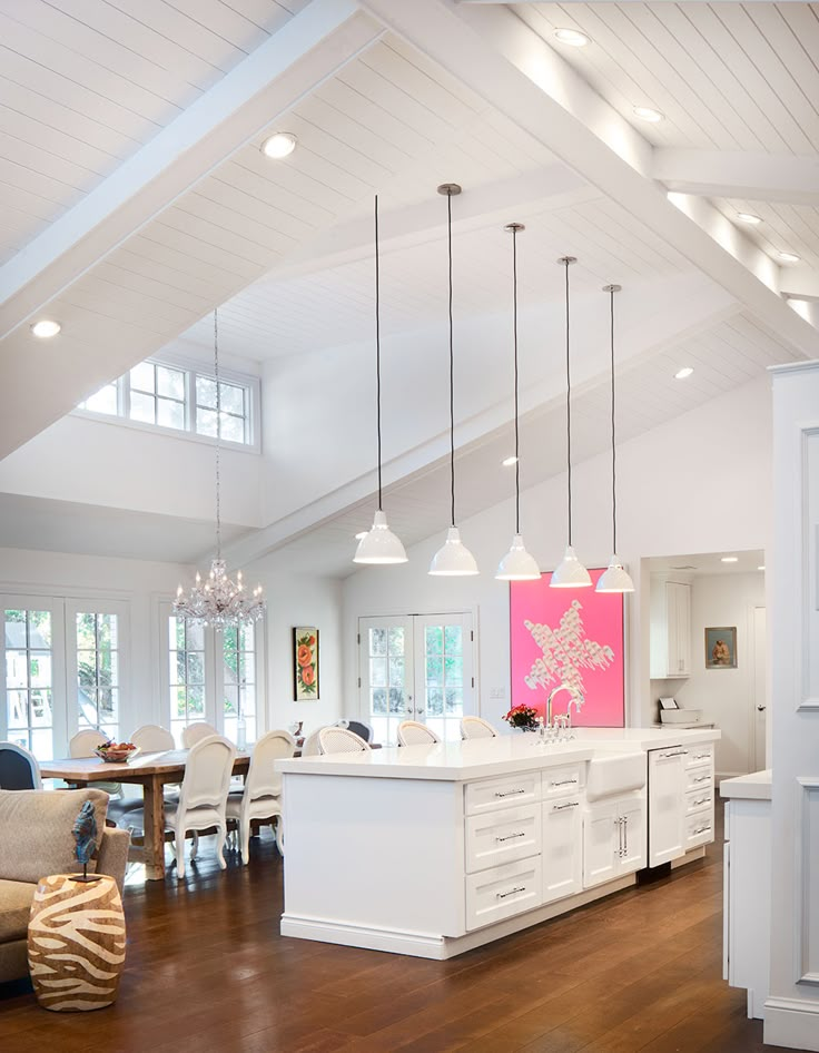 a large open concept kitchen and dining room with white cabinets, wood floors and high ceilings