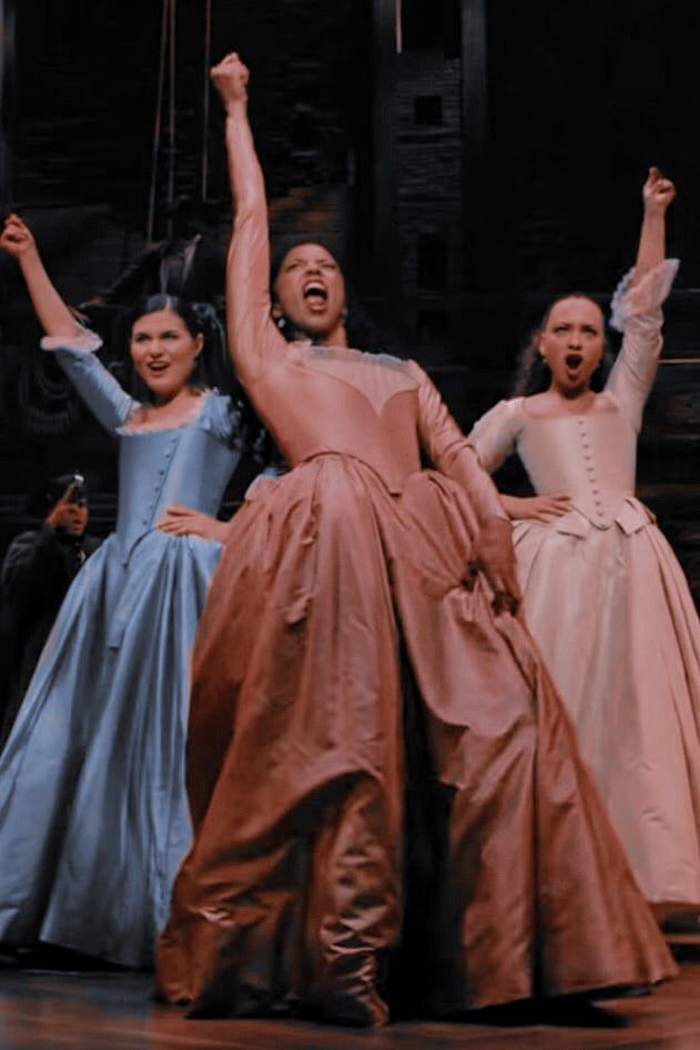 three women in long dresses are dancing on stage