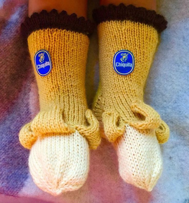 a pair of yellow knitted socks with brown trims and feet on a blanket