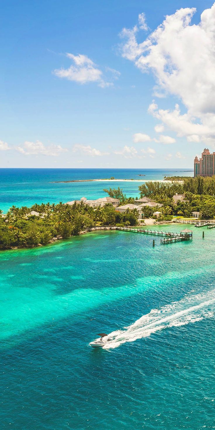 a boat traveling through the ocean near an island with palm trees and hotels in the background