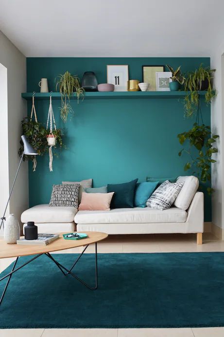 a living room with green walls and white couches, potted plants on the shelves