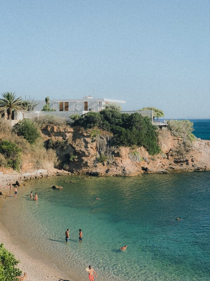 people are swimming in the clear blue water near a beach with cliffs and houses on it