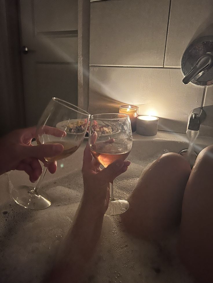 two people toasting wine glasses in a bathtub