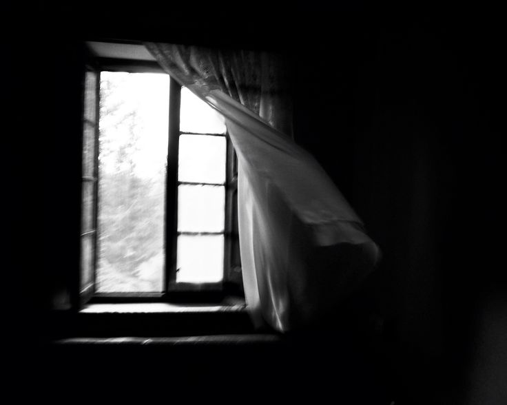 an open window in a dark room with curtains hanging from it's windowsill