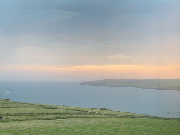 a grassy field next to the ocean with a house in the distance on top of it