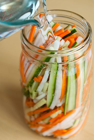 a glass jar filled with sliced up veggies and being drizzled with water