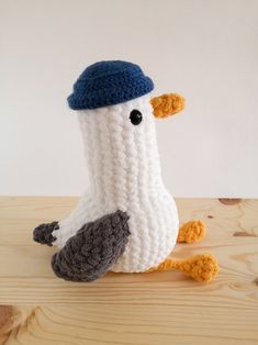 a crocheted bird with a blue hat sitting on a wooden table next to a white wall