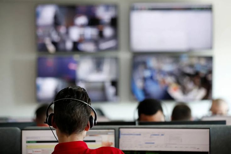 a young boy wearing headphones sitting in front of two computer monitors with television screens behind him